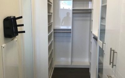 A contemporary narrow walk‑in closet featuring glass‑front cabinetry and sleek built‑in storage.